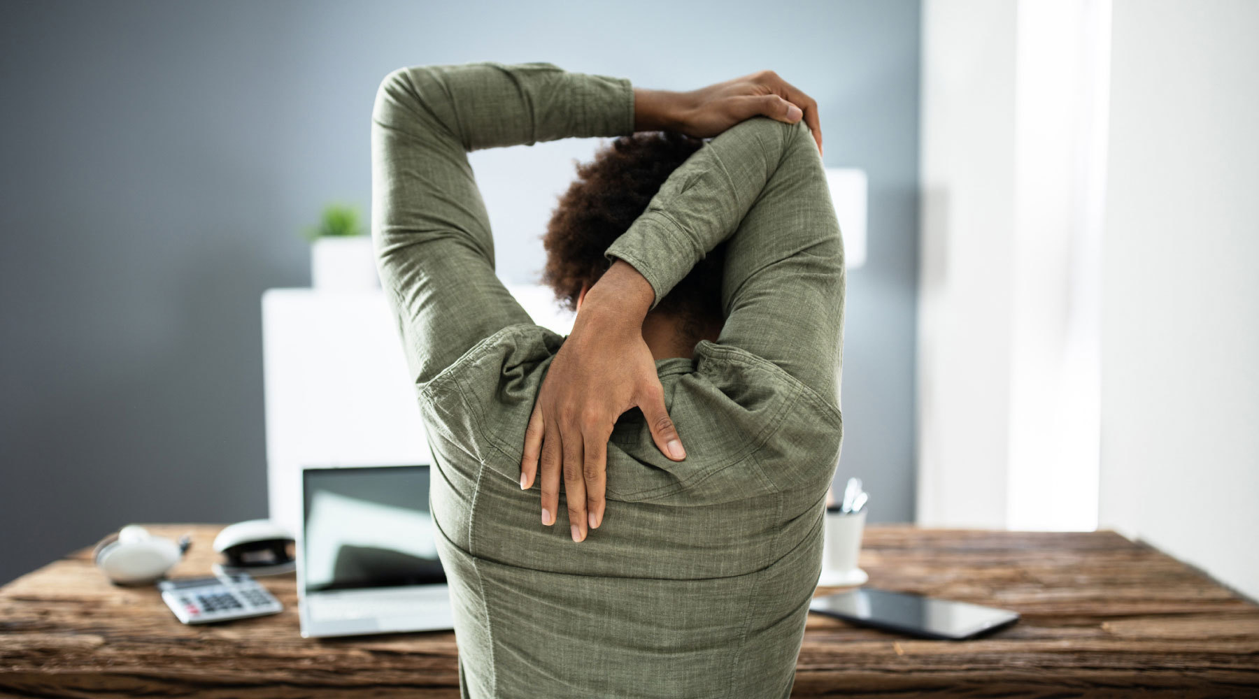 Woman stretches at desk as part of daily stretching routine.